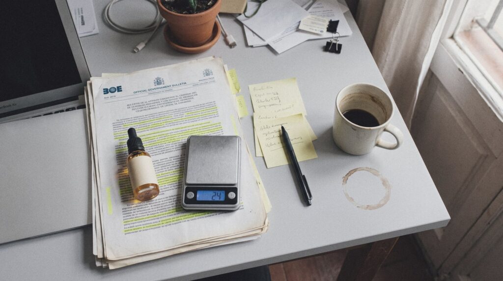 Escritorio con páginas impresas de un boletín oficial subrayadas con fosforito, un frasco pequeño de aceite de CBD y una báscula de cocina