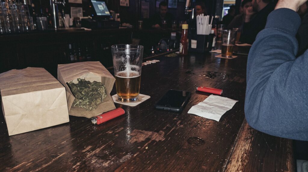 Dos bolsitas de papel con flores secas de cáñamo sobre la barra de un bar, junto a una caña de cerveza