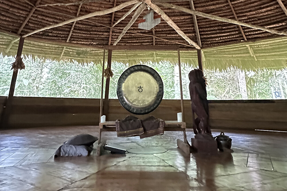 Interior de la maloca ceremonial de White Rabbit Collective con gong tradicional, selva amazónica peruana visible al fondo