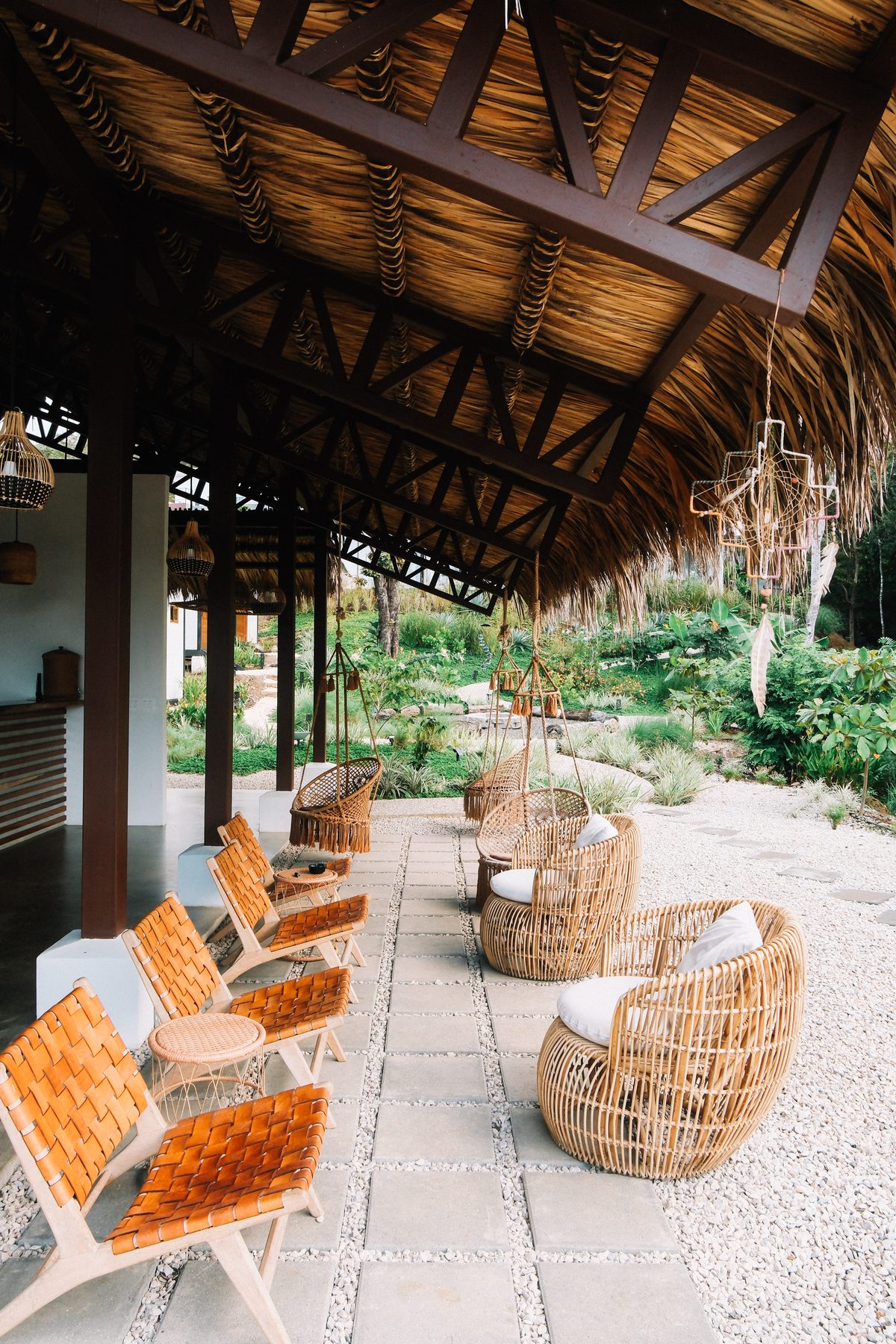 Zona de estar techada de Ananda Lodge con mobiliario de mimbre y jardín tropical